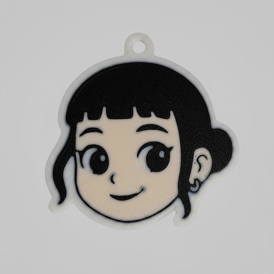 A 3D printed keychain of Zoey from K-Pop Demon Hunter. The design shows Zoey’s smiling face with short black hair, bangs, and a small earring. The keychain has a white outline with a small loop at the top for attaching to keys or bags.