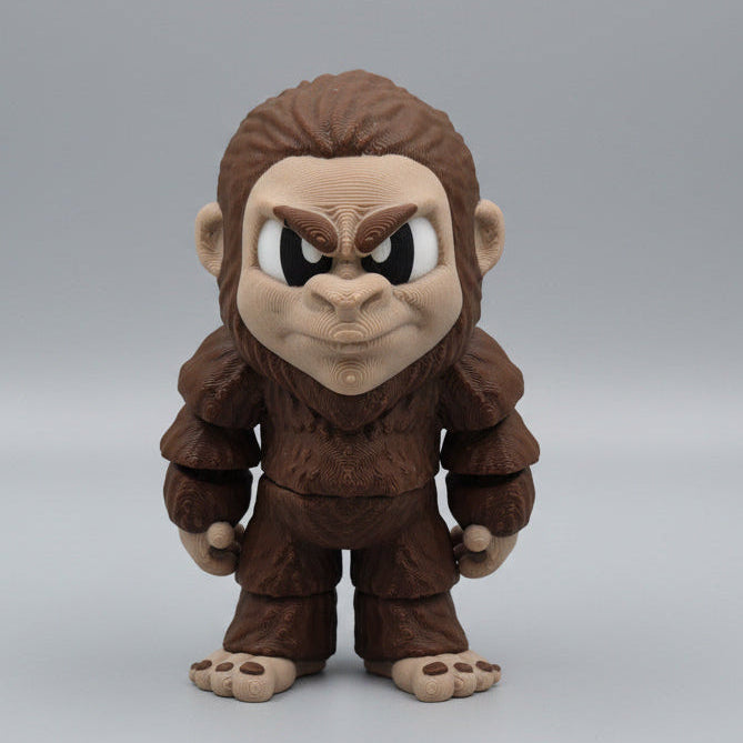 3D printed Big Foot figurine standing upright with a grumpy expression, textured brown fur, and large feet, displayed on a tabletop.