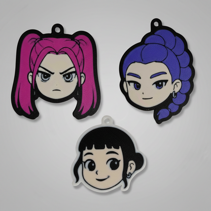 3D printed keychains of the K-Pop Demon Hunter trio – Mira with pink twin tails and a fierce expression, Rumi with long purple braided hair and a confident smile, and Zoey with short black hair and a cheerful expression. All three characters are displayed together on a dark background.