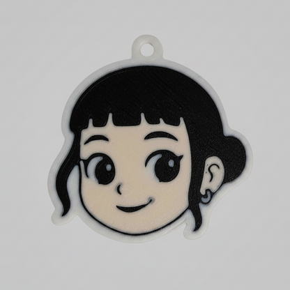 A 3D printed keychain of Zoey from K-Pop Demon Hunter. The design shows Zoey’s smiling face with short black hair, bangs, and a small earring. The keychain has a white outline with a small loop at the top for attaching to keys or bags.