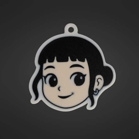 A 3D printed keychain of Zoey from K-Pop Demon Hunter. The design shows Zoey’s smiling face with short black hair, bangs, and a small earring. The keychain has a white outline with a small loop at the top for attaching to keys or bags.