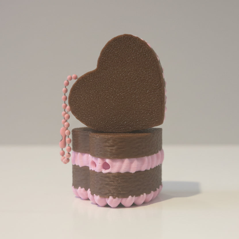 Small figurine with a heart-shaped top and pink base, set against a background of other similar figurines.