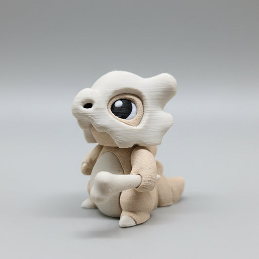 3D printed Cubone flexi figure in light beige tones, shown from a front-left angle holding a small bone, featuring large glossy eyes, a skull helmet, and articulated body joints on a neutral grey background