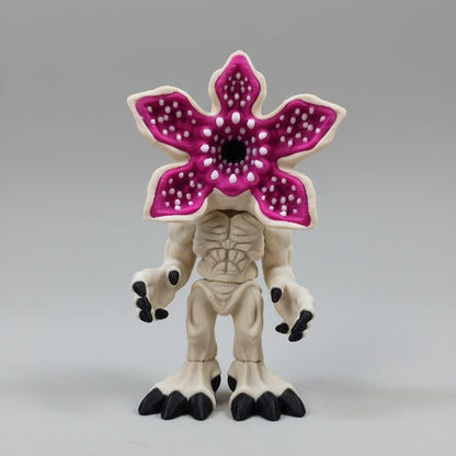 Front view of a filament 3D printed mind flayer–inspired miniature with a pale bone-coloured body, black claws, and a large open pink flower-shaped head with detailed inner petal texture, displayed on a neutral background.