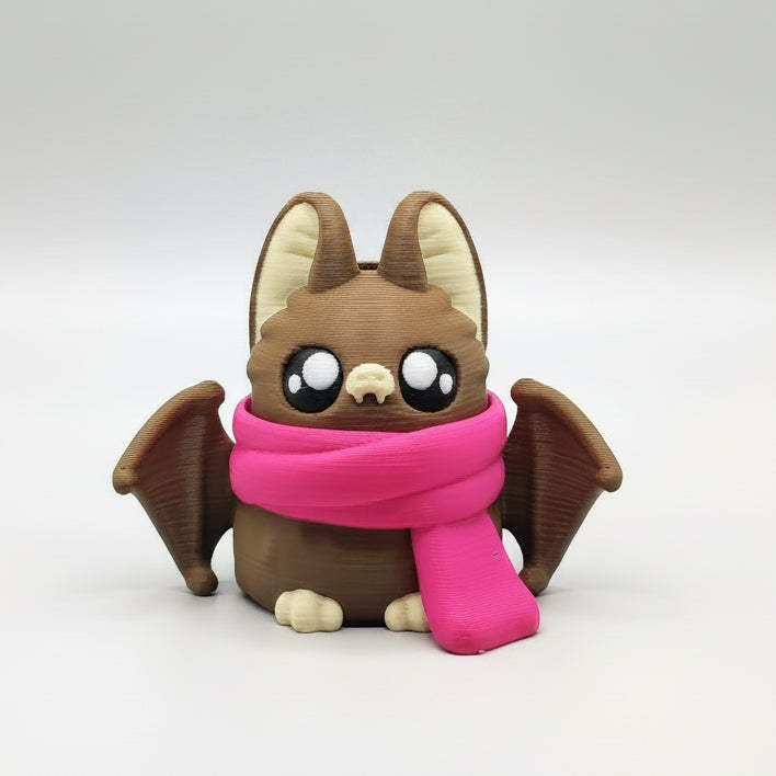A cute 3D-printed brown bat with large eyes, little wings and a bright pink scarf, sitting against a plain white background.