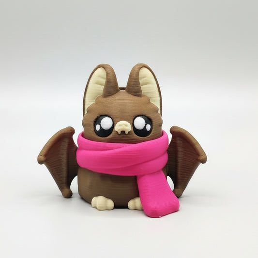 A cute 3D-printed brown bat with large eyes, little wings and a bright pink scarf, sitting against a plain white background.