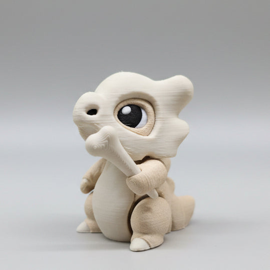 Side view of a 3D printed Cubone articulated figure sitting upright, showing layered skull helmet details, rounded body shape, and movable limbs in soft beige and cream colours
