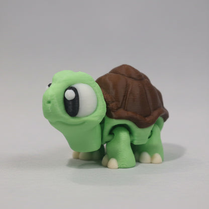 Green flexi 3D printed turtle figure with large cartoon eyes, a brown textured shell, and small cream coloured feet. Cute articulated turtle collectible displayed on a plain background.