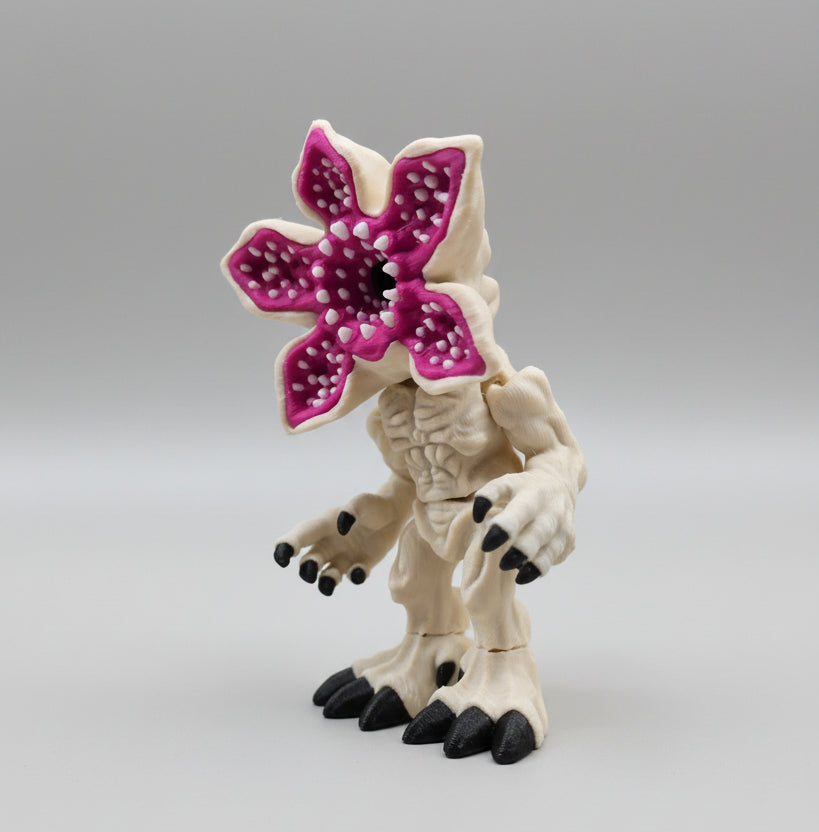 Angled view of a filament 3D printed mind flayer–style creature featuring a muscular light body, black claws, and a vibrant pink petal-like head opened wide, showing layered filament lines and sculpted detail.