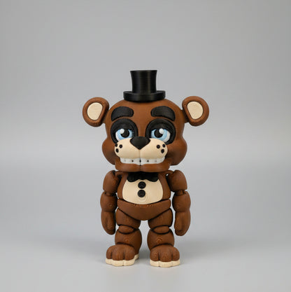 Front view of a 3D printed Freddy Fazbear flexi figure inspired by Five Nights at Freddy’s, featuring a brown animatronic bear with articulated limbs, black top hat, bow tie, blue eyes, button details, and a toothy grin, photographed against a clean light background.