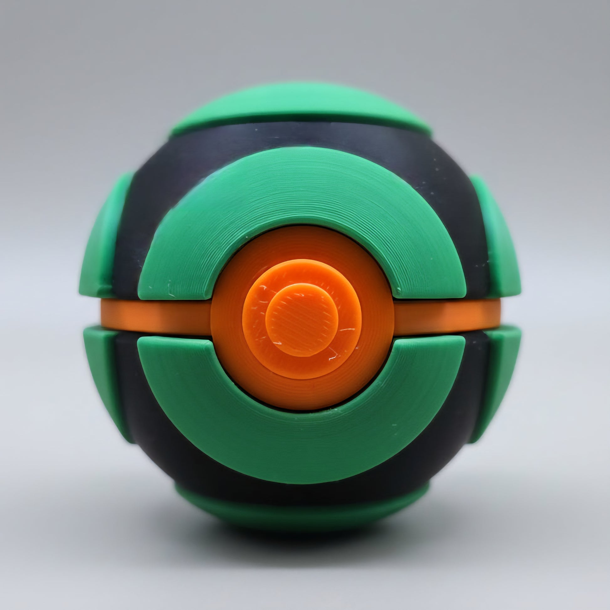 Front view of a 3D printed Dusk Ball featuring green curved panels over a black shell with a bright orange centre button and a white lower half, displayed against a neutral background.