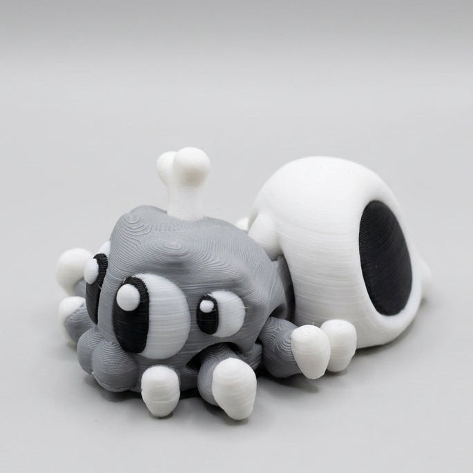 Grey 3D printed Spider Skull figurine featuring oversized black and white eyes, eight little legs with white feet, and a white skull-shaped abdomen with a bone sticking out, photographed against a light grey background.