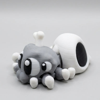 Grey 3D printed Spider Skull figurine featuring oversized black and white eyes, eight little legs with white feet, and a white skull-shaped abdomen with a bone sticking out, photographed against a light grey background.