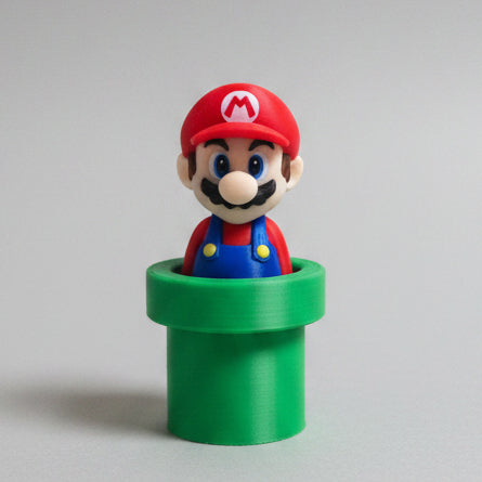 3D printed collectible of Mario emerging from a classic green warp pipe, featuring his red hat, blue overalls, moustache, and smiling face against a light grey background.