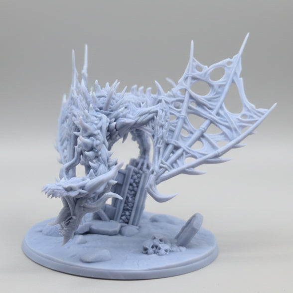 Front-angle view of a detailed unpainted fantasy dragon arch miniature with curved horns, ribbed wings, and ruins on the base.