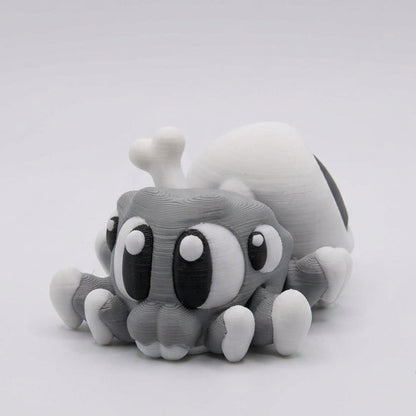 Side view of a cute grey 3D printed Spider Skull figurine showing large expressive eyes, small white-tipped legs, and a rounded white skull-shaped abdomen with a large black hollow eye socket, against a light grey background.