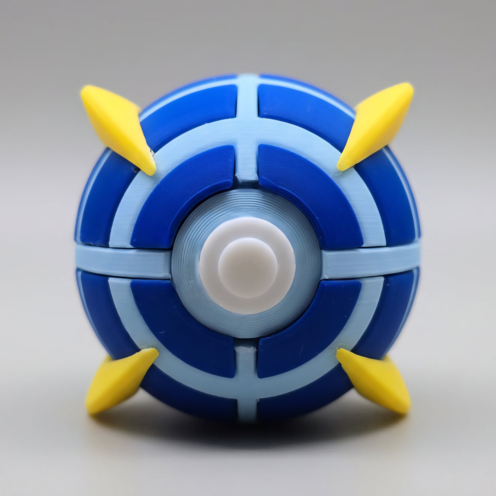 Front view of a 3D printed Beast Ball featuring dark blue and light blue segmented panels, white centre button, and four yellow spike accents on a clean white background.