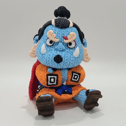 Side view of a 3D printed knitted-style Jinbe figure inspired by One Piece, showing his blue skin, orange outfit, red cape and brown sandals.